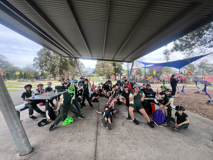 A group photo of students some wearing helmets sitting on chairs and the floor at the bicycle education centre.
