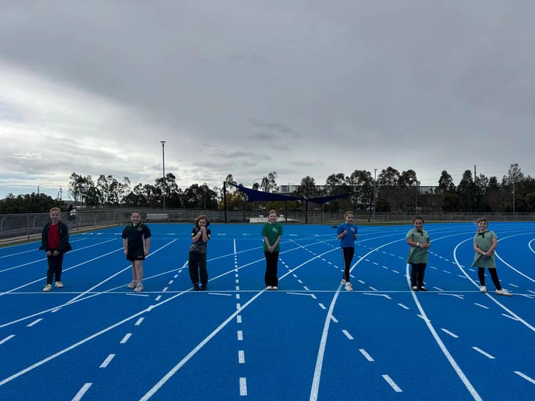 7 students about to start a race on a bright blue athletics track at the athletics carnival.