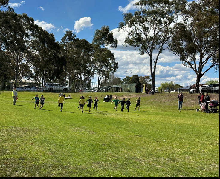 A number of students running on the oval participating in a fun run on the green grass.