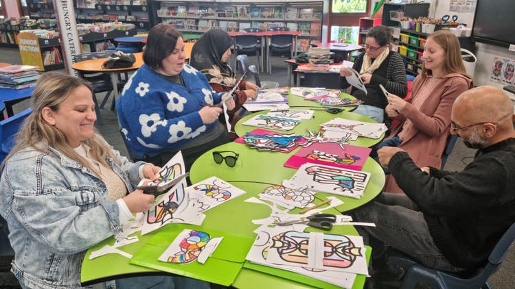 A group of parent volunteers sitting around a green table cutting childrens artwork for the education week display.